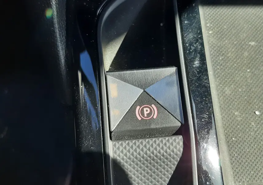 Gros plan sur le bouton de frein à main électrique noir avec symbole rouge dans l'habitacle du DS3 Crossback gris foncé.