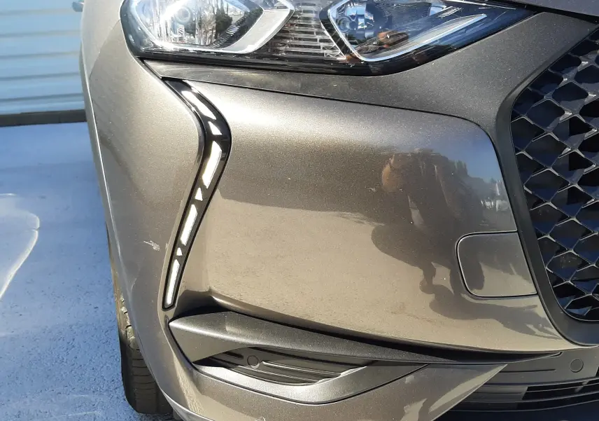 Gros plan sur l'avant droit gris foncé du DS3 Crossback 2021, mettant en valeur le phare et la calandre distinctive.