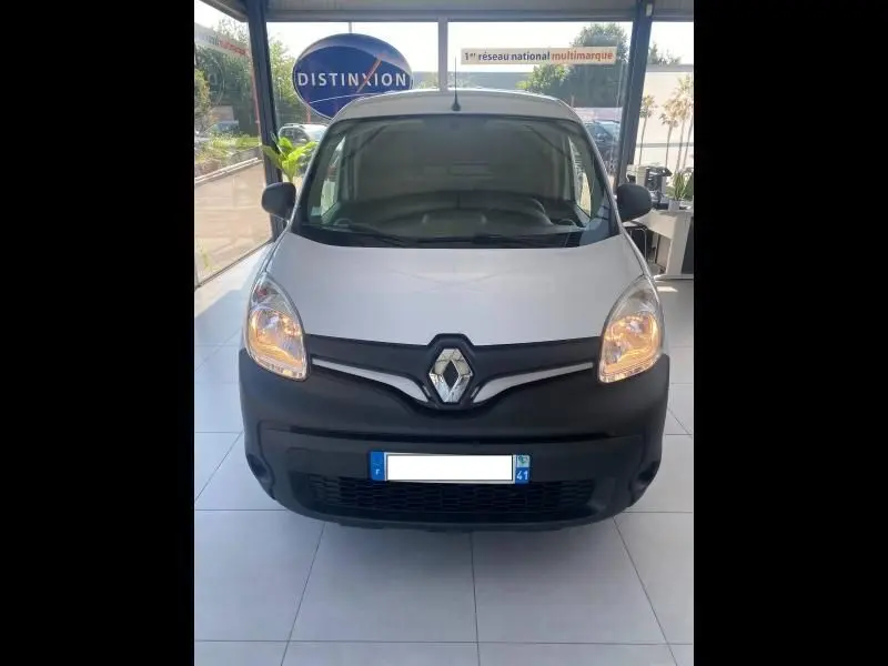 Vue avant d’un Renault Kangoo Express blanc 2022 avec pare-chocs noir et phares allumés en showroom.