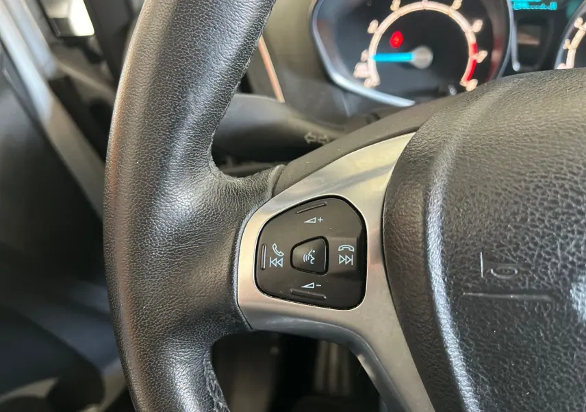 Gros plan sur le volant en cuir noir du Ford B-MAX 2015 avec commandes audio intégrées et tableau de bord lumineux.