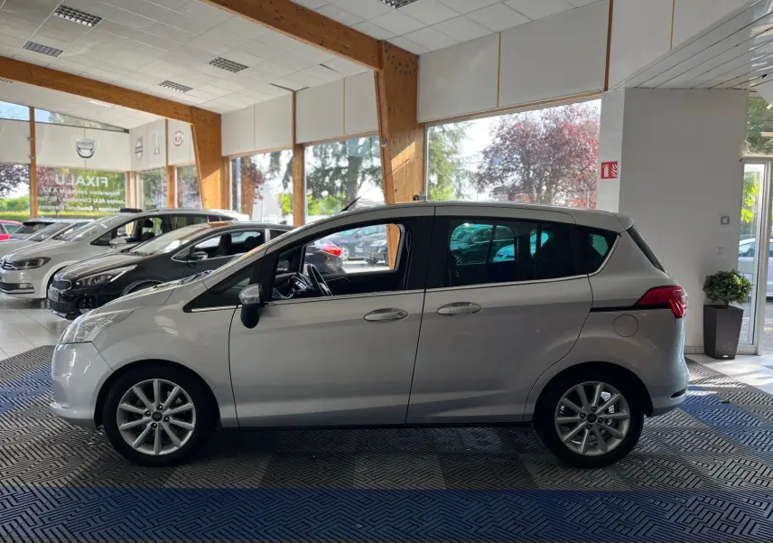 Ford B-MAX gris clair vue de profil côté gauche dans un showroom lumineux avec jantes alliage visibles.