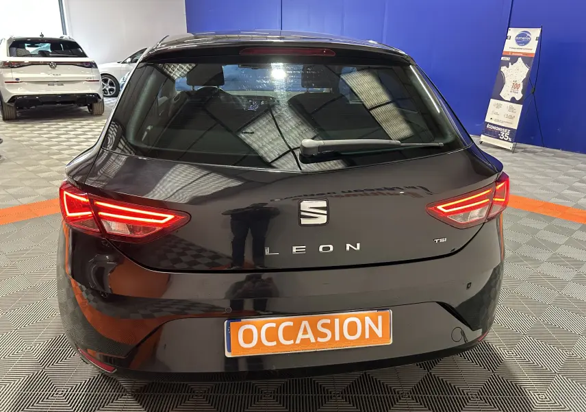 Vue arrière d'une SEAT Leon noire de 2014 avec feux allumés, plaque "OCCASION" en intérieur de showroom.