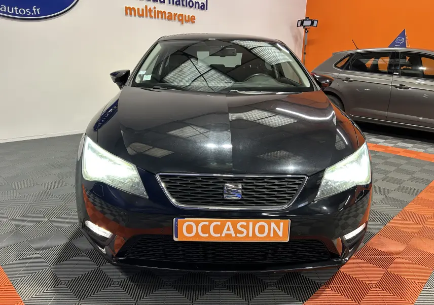 Vue frontale d'une SEAT Leon noire de 2014 avec phares allumés et plaque "OCCASION" en orange.