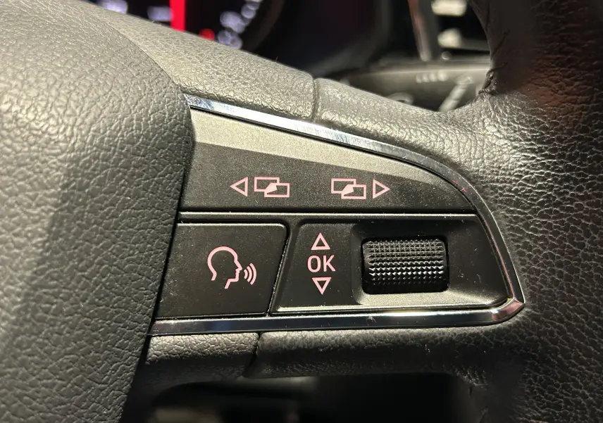 Gros plan sur les commandes multifonctions à gauche du volant noir du SEAT LEON 2014, boutons de navigation et reconnaissance vocale.