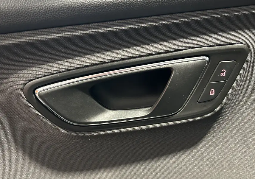 Poignée intérieure de porte noire avec encadrement chromé et boutons de verrouillage éclairés sur une SEAT LEON 2014.