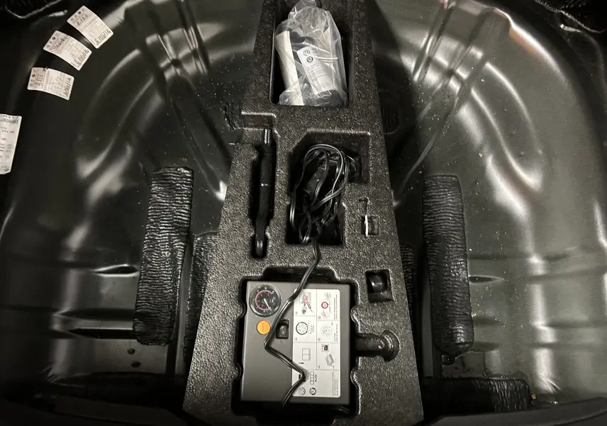 Vue plongeante sur le compartiment de roue de secours d'une SEAT Leon noire avec kit de réparation et accessoires rangés.