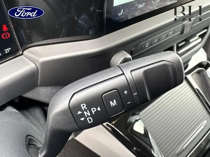 Gros plan intérieur sur le levier de vitesses automatique noir du Ford Transit Custom gris, avec tableau de bord et écran tactile en arrière-plan.