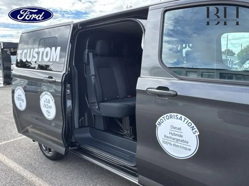 Vue latérale gauche du Ford Transit Custom gris métallisé avec porte coulissante ouverte révélant les sièges noirs à l'intérieur.