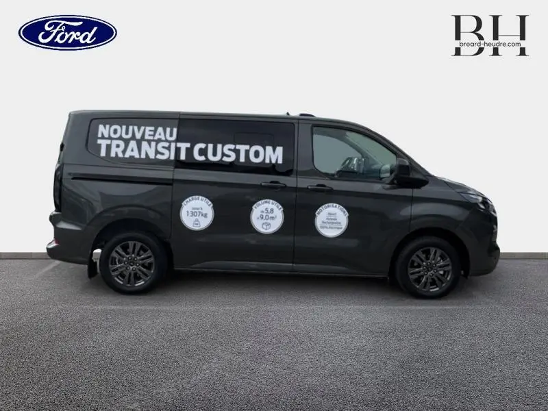 Vue de profil droit du Ford Transit Custom Fourgon gris métallisé avec marquage publicitaire blanc sur la carrosserie.
