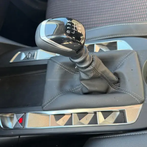 Gros plan sur le levier de vitesse manuel noir du DS3 100 BVM6 Performance Line 2024, avec console centrale en cuir gris et boutons argentés.