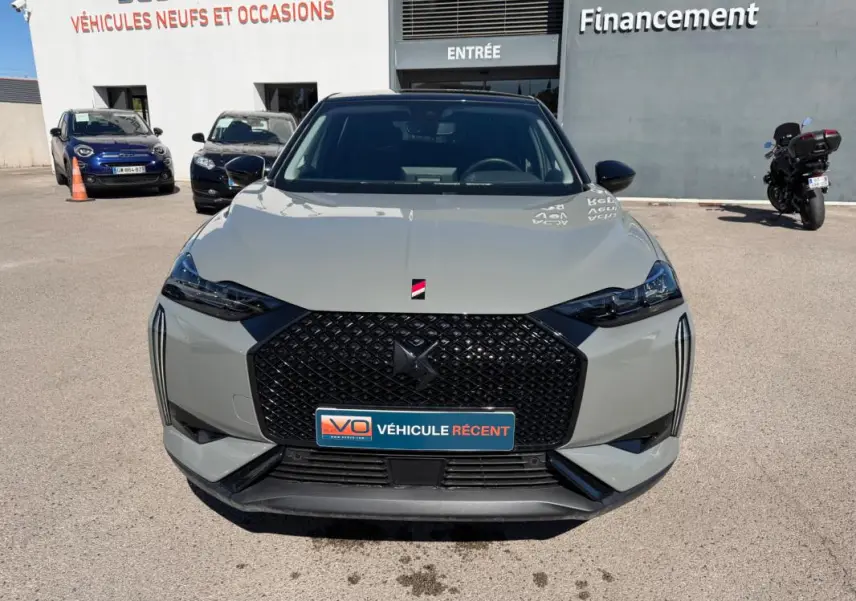 Vue frontale d’une DS3 100 BVM6 Performance Line gris 2024 avec calandre noire et phares étirés, en extérieur devant un concessionnaire.