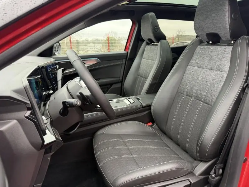 Vue intérieure côté conducteur du Renault Austral 2025 rouge Flamme, sièges gris avec surpiqûres blanches et toit panoramique.