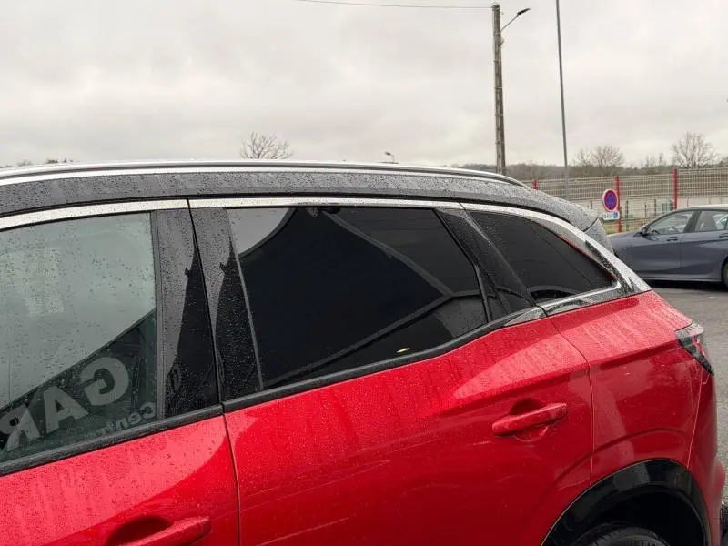 Vue latérale droite du Renault Austral 2025 rouge flamme, mettant en valeur les vitres teintées et la carrosserie brillante sous la pluie.