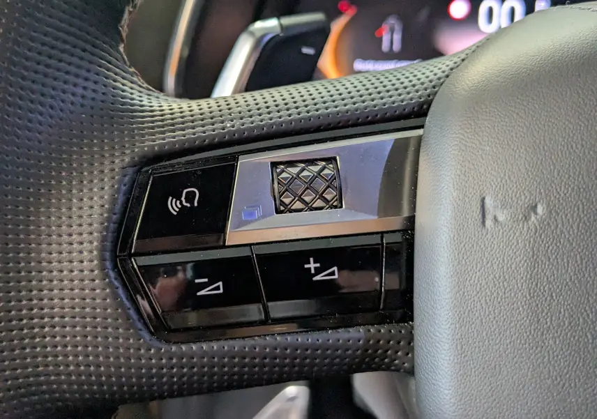 Gros plan sur les commandes au volant côté gauche du DS7 gris laqué, avec boutons de volume et fonction mains libres.