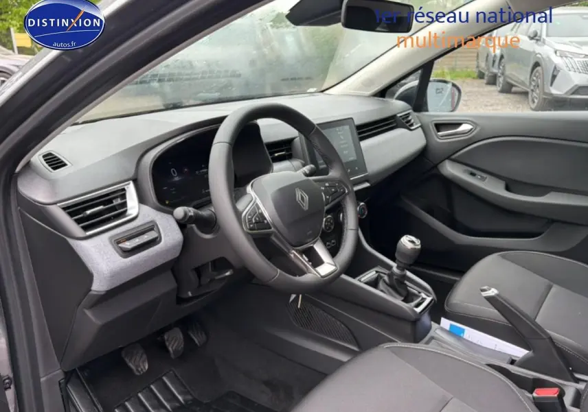 Vue intérieure côté conducteur de la Renault Clio V gris schiste, avec volant multifonction et boîte manuelle visible.