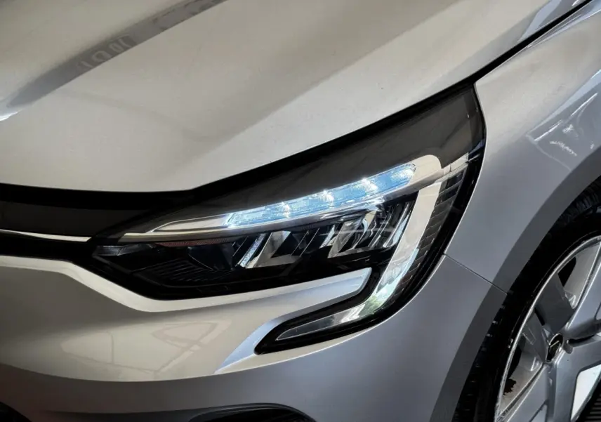 Gros plan sur le phare avant droit allumé d'une Renault Clio Business TCe 90 gris clair, avec partie de la roue visible.