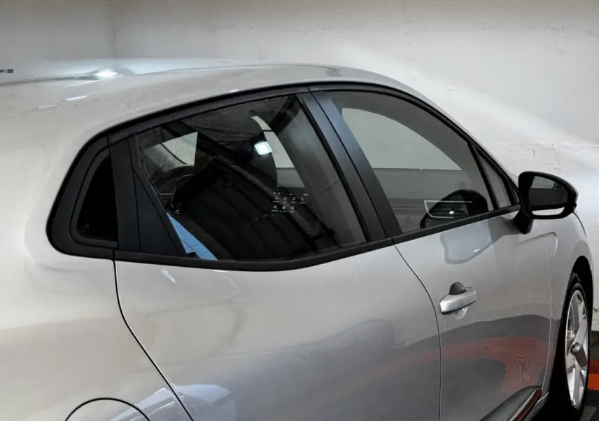 Profil droit d'une Renault Clio Business TCe 90 gris clair, avec poignées de porte intégrées et vitres teintées.