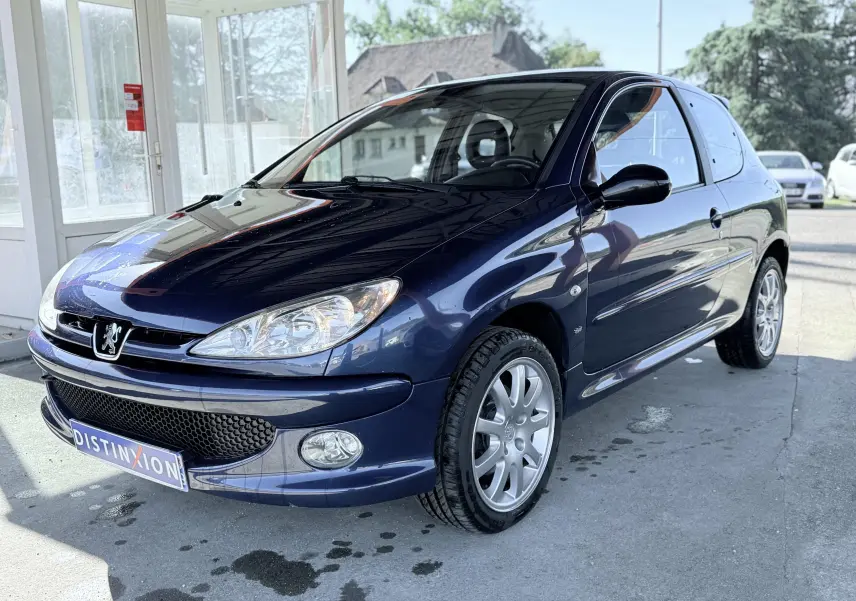 Peugeot 206 bleu en 3/4 avant droit, avec jantes alliage et phares clairs sous lumière naturelle.