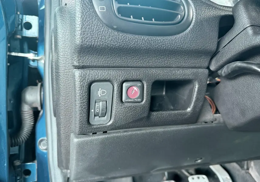 Détail intérieur côté gauche d’un Peugeot 206 bleu, montrant les commandes de réglage des phares et désactivation de l’airbag passager.