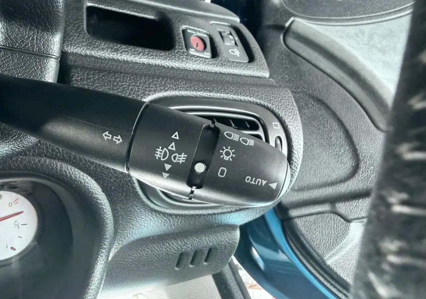 Gros plan sur la commande des feux et clignotants dans l’habitacle noir d’une Peugeot 206 bleu, côté gauche du volant.