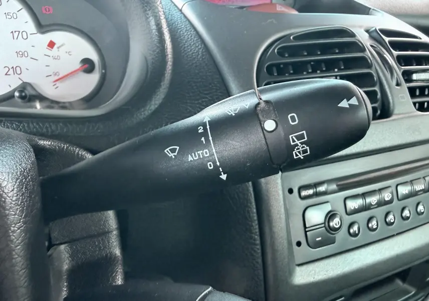 Gros plan sur la commande d’essuie-glace côté gauche du tableau de bord noir d’une Peugeot 206 bleue de 2003.