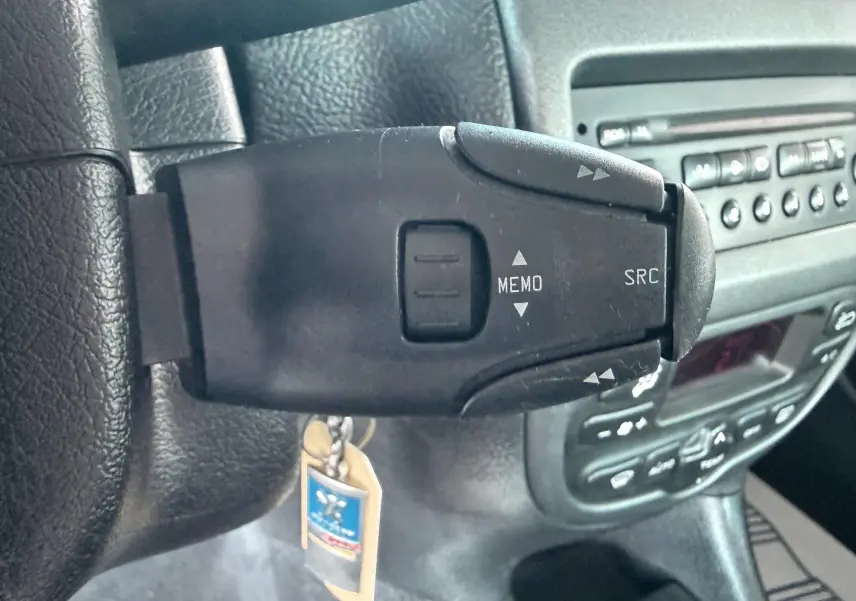 Gros plan sur la commande au volant gauche d’une Peugeot 206, avec tableau de bord et autoradio en arrière-plan.