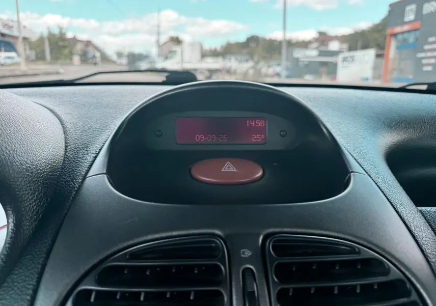 Tableau de bord central de Peugeot 206 bleu, affichage digital rouge avec horloge et température, bouton warning rouge visible.