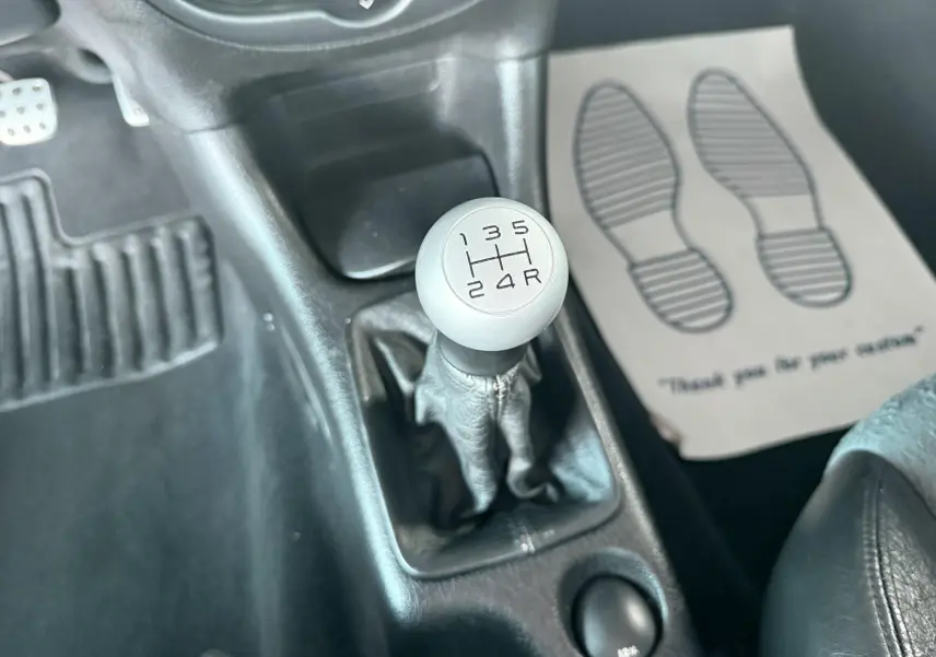 Gros plan sur le levier de vitesses manuel gris dans l’habitacle noir d’une Peugeot 206, avec tapis de sol visible.