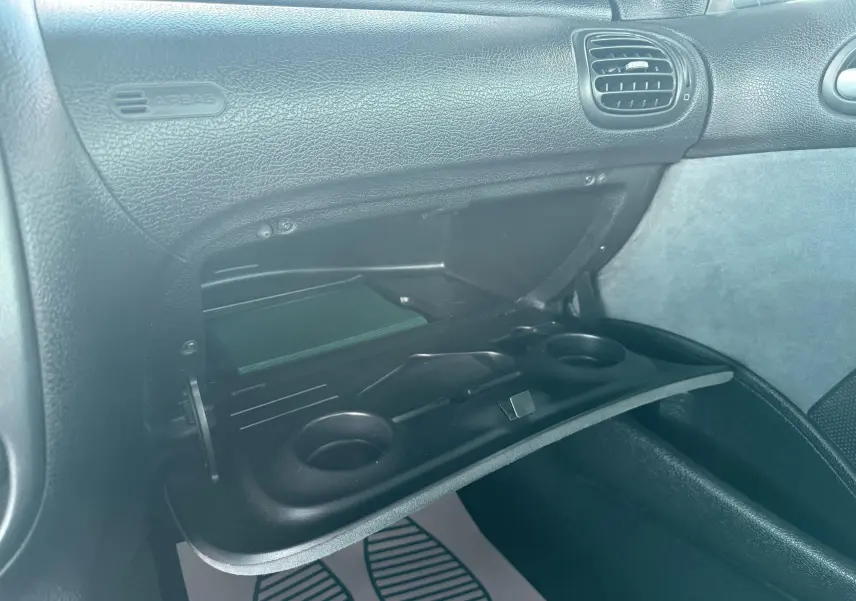 Intérieur de la Peugeot 206 bleu de 2003, vue rapprochée de la boîte à gants ouverte avec porte-gobelets intégrés.