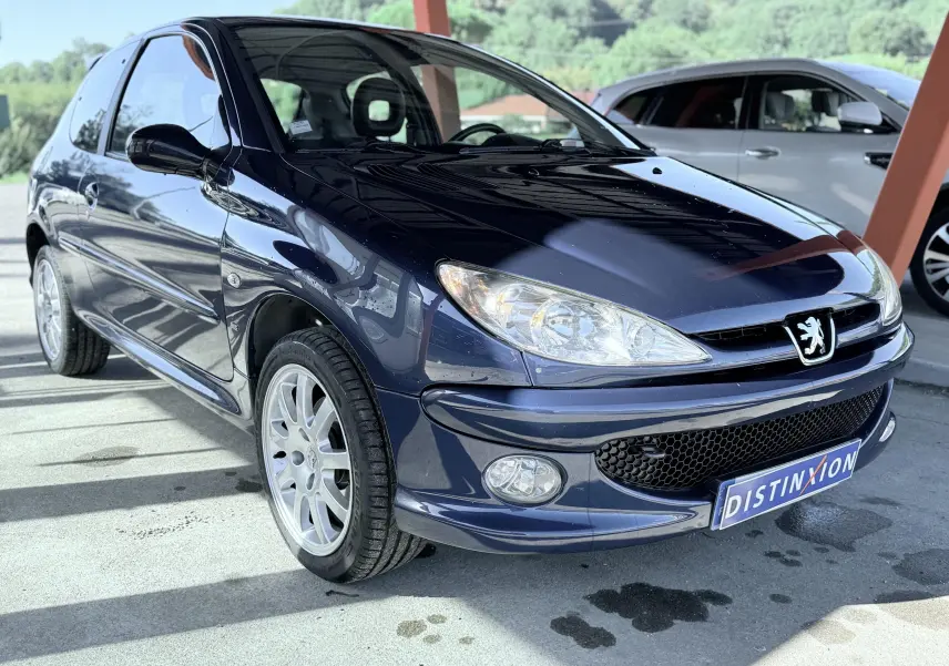 Peugeot 206 bleu vue 3/4 avant droit, sous abri avec jantes alliage et plaque "DISTINXION" visible.