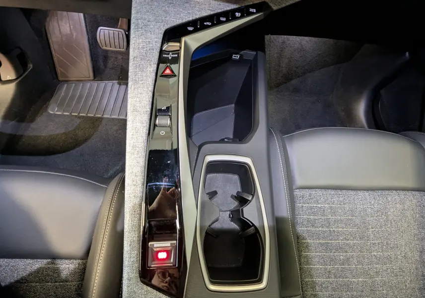 Vue intérieure plongeante sur la console centrale noire du Peugeot 3008 Hybrid 145 avec porte-gobelets et tissu gris embossé.