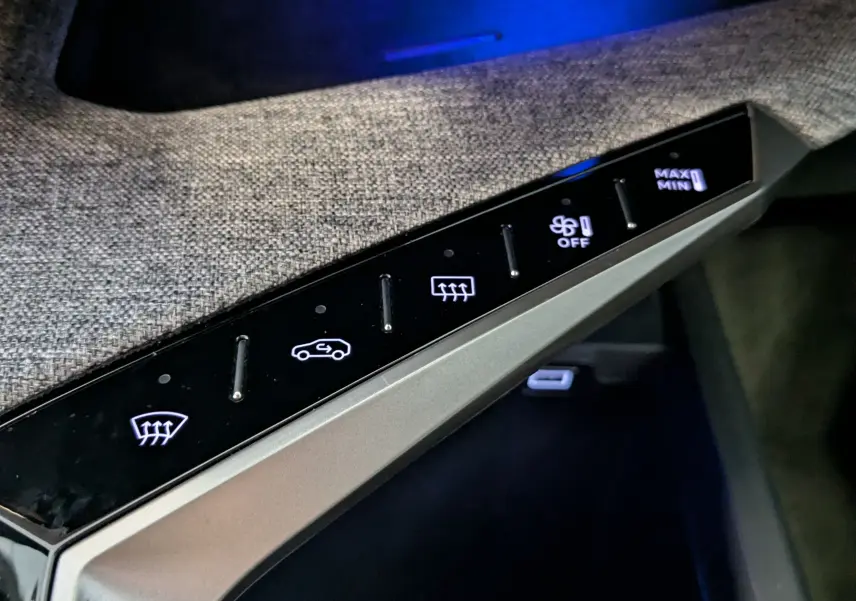 Gros plan sur les commandes tactiles noires de la console centrale, avec tissu gris texturé en arrière-plan dans un Peugeot 3008 noir.