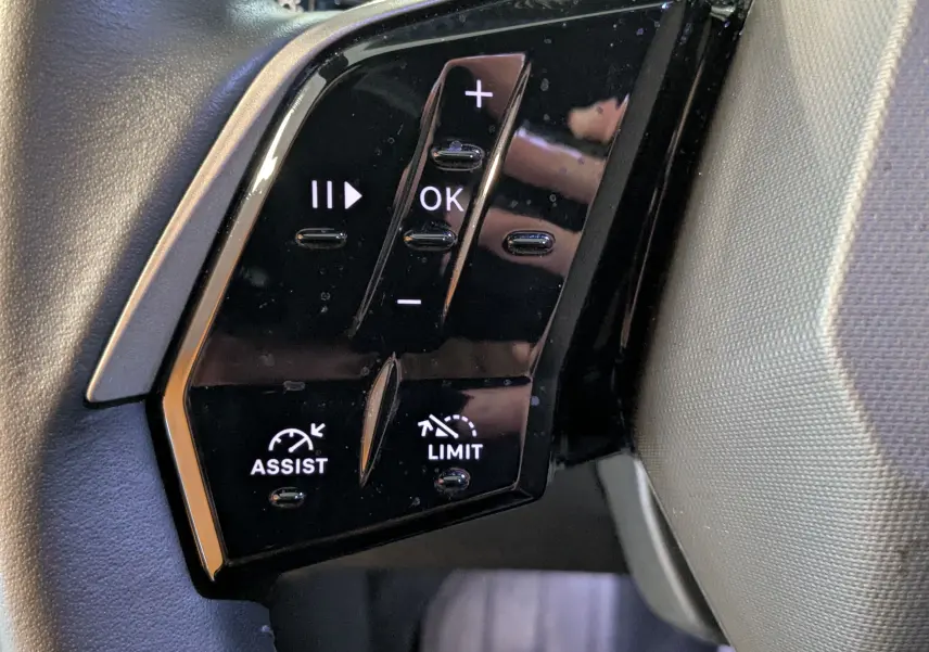 Gros plan sur les commandes noires du volant cuir du Peugeot 3008 Hybrid 145, avec boutons de régulateur et assistant.