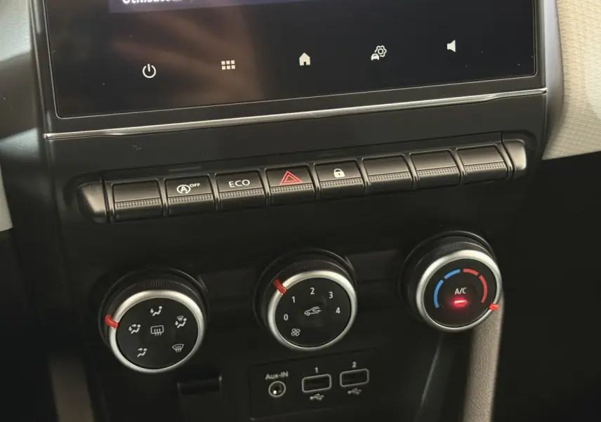 Gros plan sur les commandes de climatisation et boutons fonctionnels du tableau de bord central de la Renault Clio blanche Evolution TCe 100 GPL 2023.