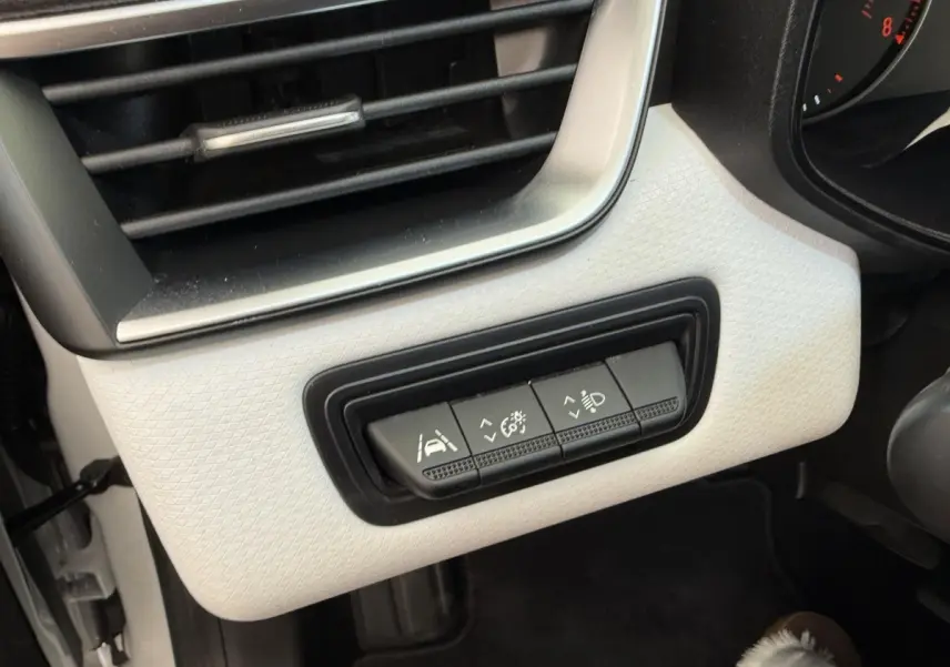 Gros plan sur les commandes d'assistance et éclairage sur tableau de bord blanc côté conducteur d'une Renault Clio 2023.