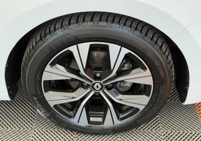 Gros plan sur la roue avant droite d’une Renault Clio blanche, avec jante alliage noire et argentée au design moderne.
