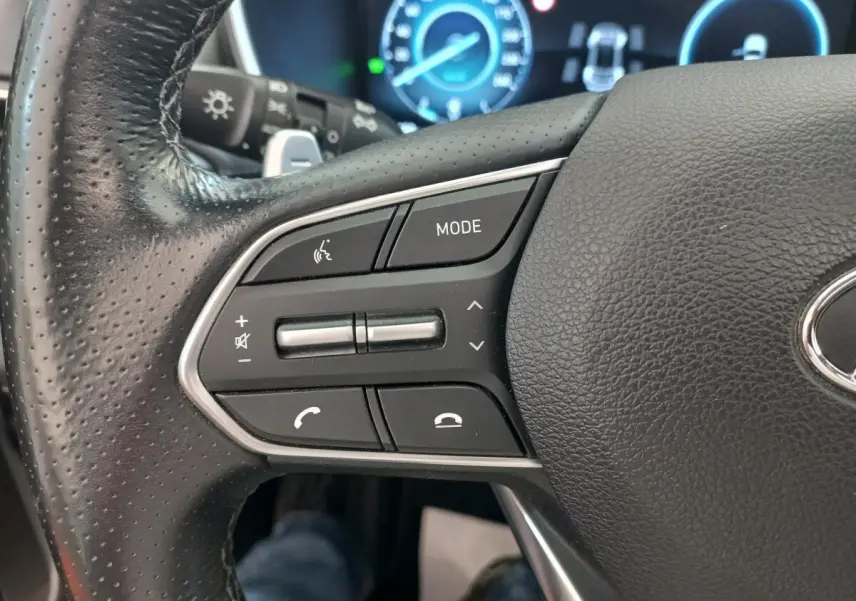Gros plan sur le volant cuir noir du Hyundai Santa Fe 2022, avec commandes multifonctions et tableau de bord numérique bleu.