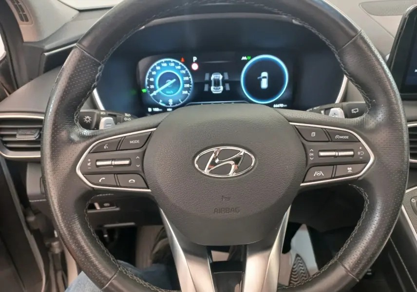 Vue rapprochée du volant cuir multifonctions du Hyundai Santa Fe 2022 avec tableau de bord numérique éclairé.