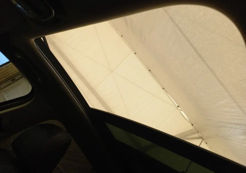 Vue intérieure du toit ouvrant électrique en verre du Hyundai Santa Fe gris clair, avec store déployé.