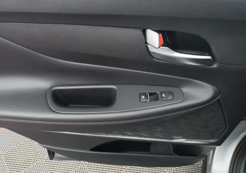 Vue rapprochée de la porte intérieure côté gauche du Hyundai Santa Fe gris clair avec commandes de verrouillage et poignée argentée.