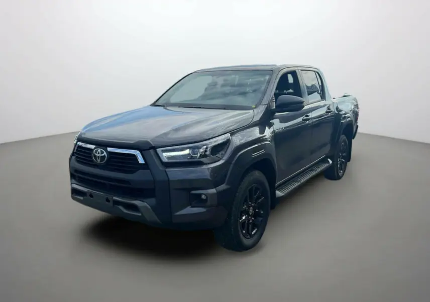 Toyota Hilux 2025 gris atlas en 3/4 avant droit, avec calandre noire et jantes alliage sombres.