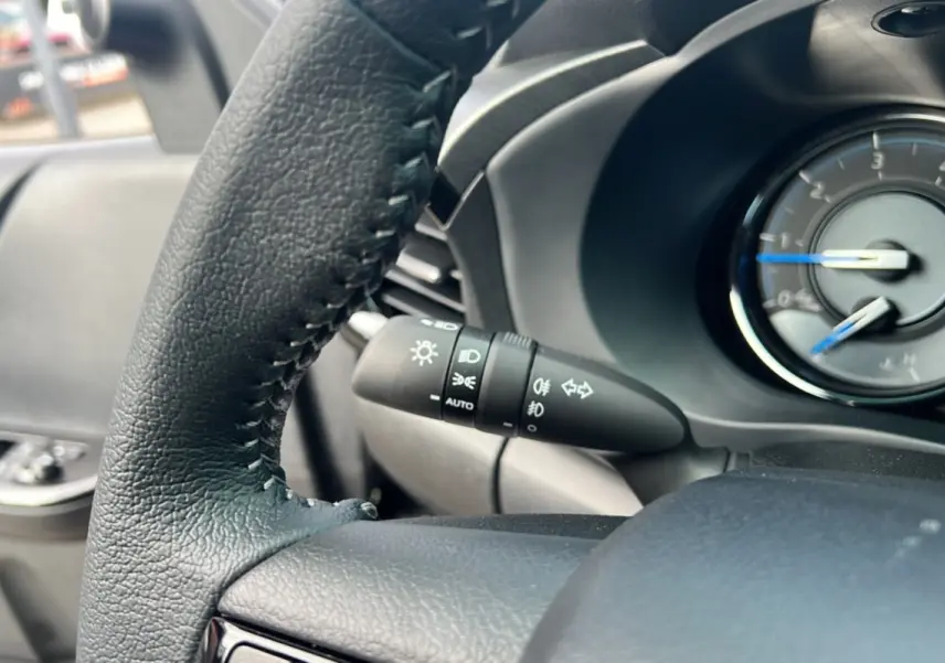 Gros plan sur le volant et le commodo des phares du Toyota Hilux 4x4 gris atlas, version Invincible 2025.