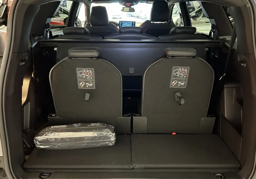 Vue arrière du coffre du Peugeot 5008 gris Platinium 2024 avec sièges rabattus et kit de sécurité visible.