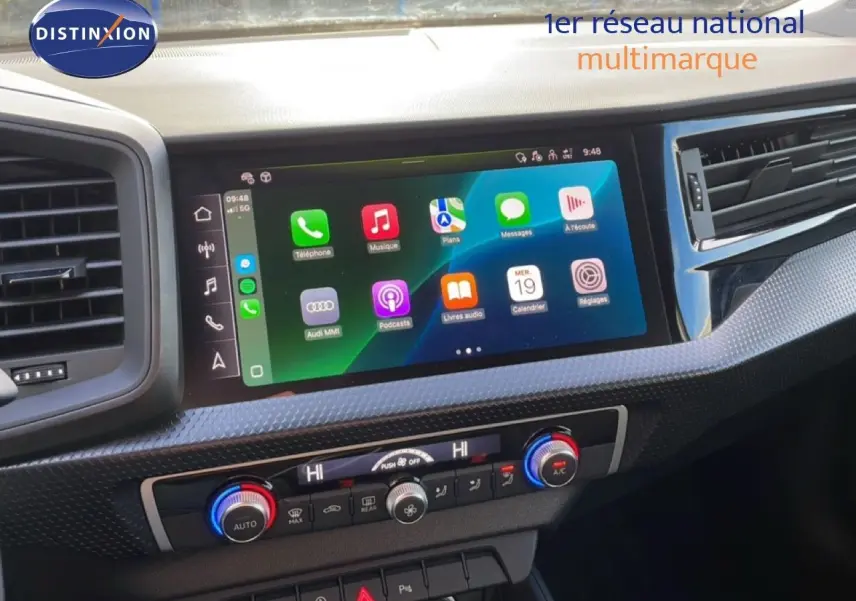 Coffre ouvert d'une Audi A1 Sportback blanc glacier métal, vue arrière montrant l'espace de chargement vide avec tapis noirs.