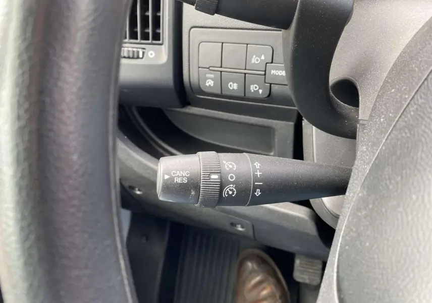 Gros plan sur la commande de régulateur de vitesse à gauche du volant dans l'habitacle noir de l'Opel Movano blanc.