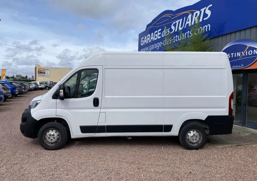 Vue de profil côté gauche d'un Opel Movano Fourgon blanc 2022 stationné devant un garage.