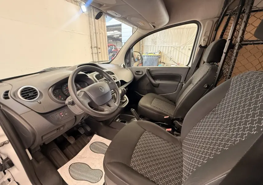 Vue intérieure côté conducteur du Renault Kangoo blanc 2016, montrant les sièges, volant et cloison tubulaire.