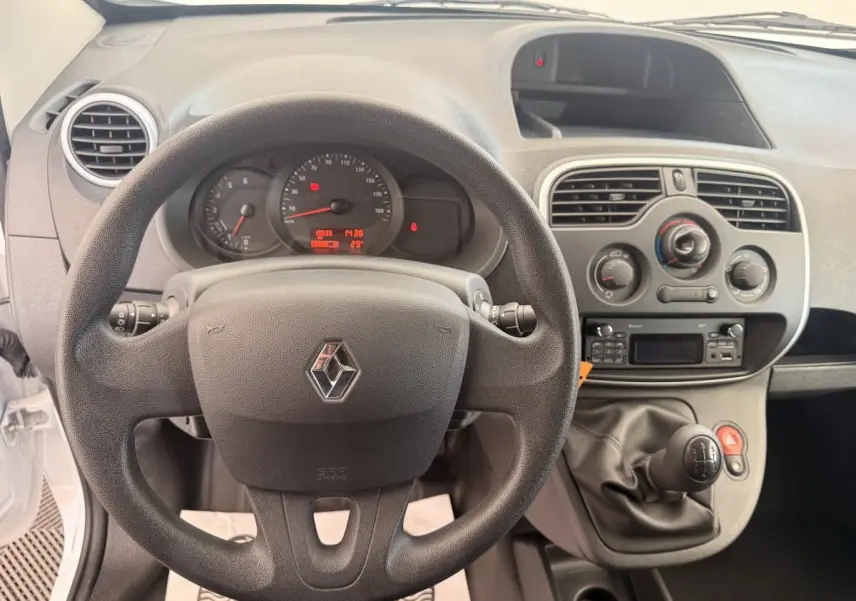 Vue intérieure centrée sur le volant et tableau de bord du Renault Kangoo blanc avec levier de vitesse manuel.