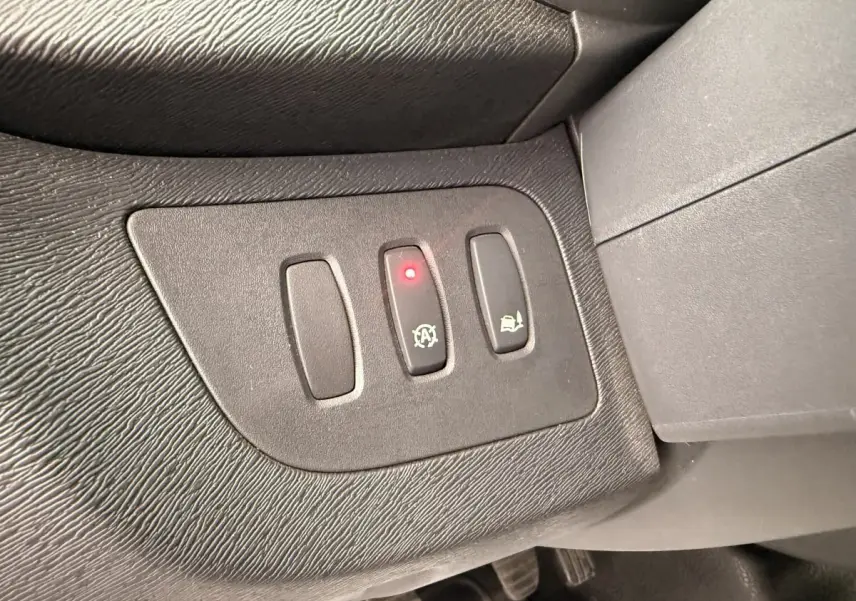 Gros plan sur les boutons de commande noirs du tableau de bord du Renault Kangoo blanc, avec témoin lumineux rouge allumé.
