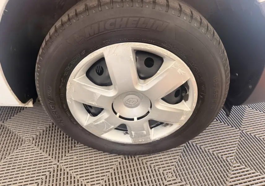Gros plan sur la roue avant gauche du Renault Kangoo blanc de 2016 avec jante acier et enjoliveur rayé.